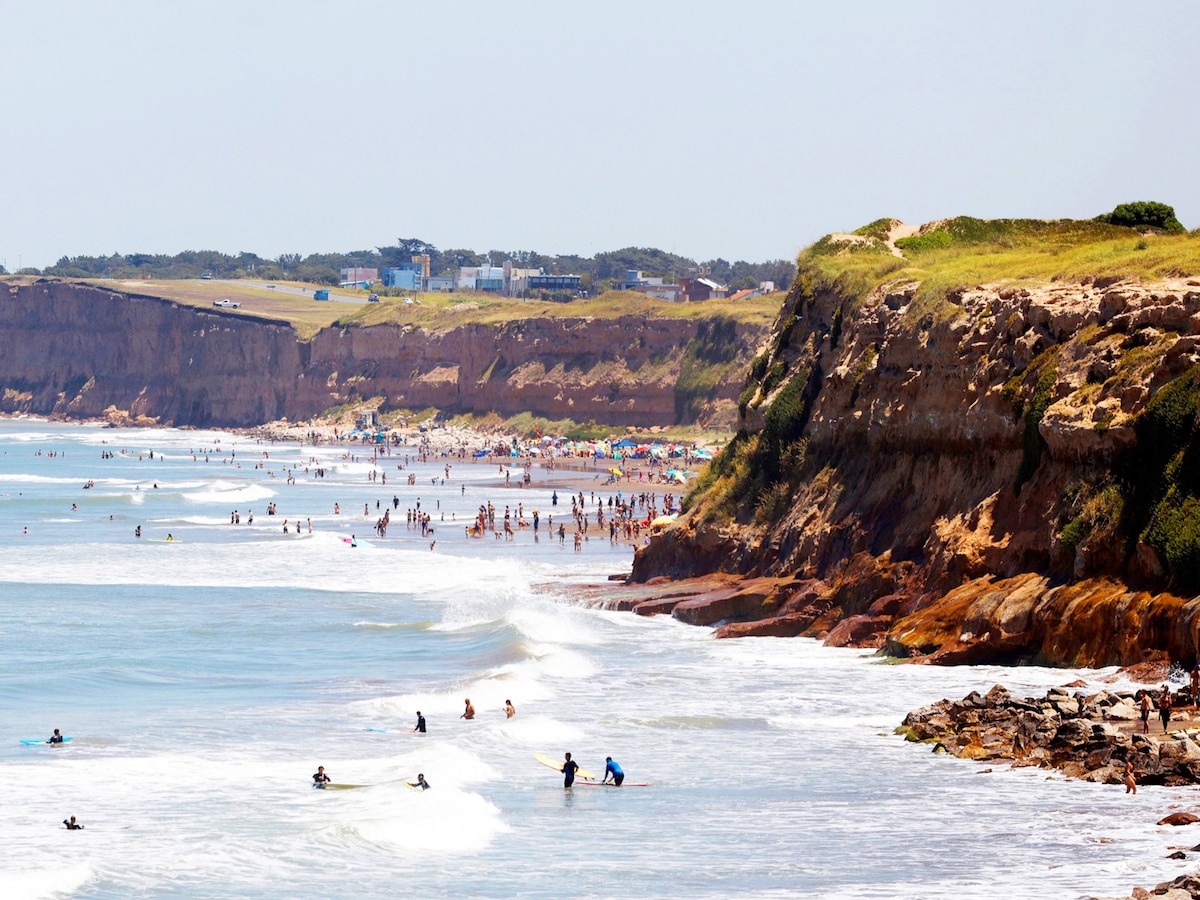 Surfistas en Playa Mogotes de Mar del Plata con acantilados verdes al fondo