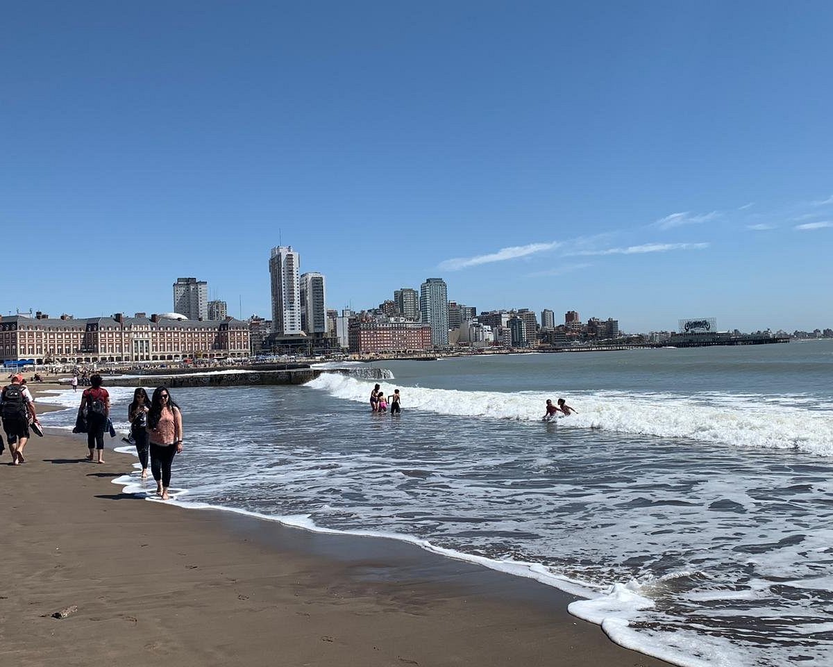 Personas caminando en la Playa Las Toscas de Mar del Plata con ciudad al fondo