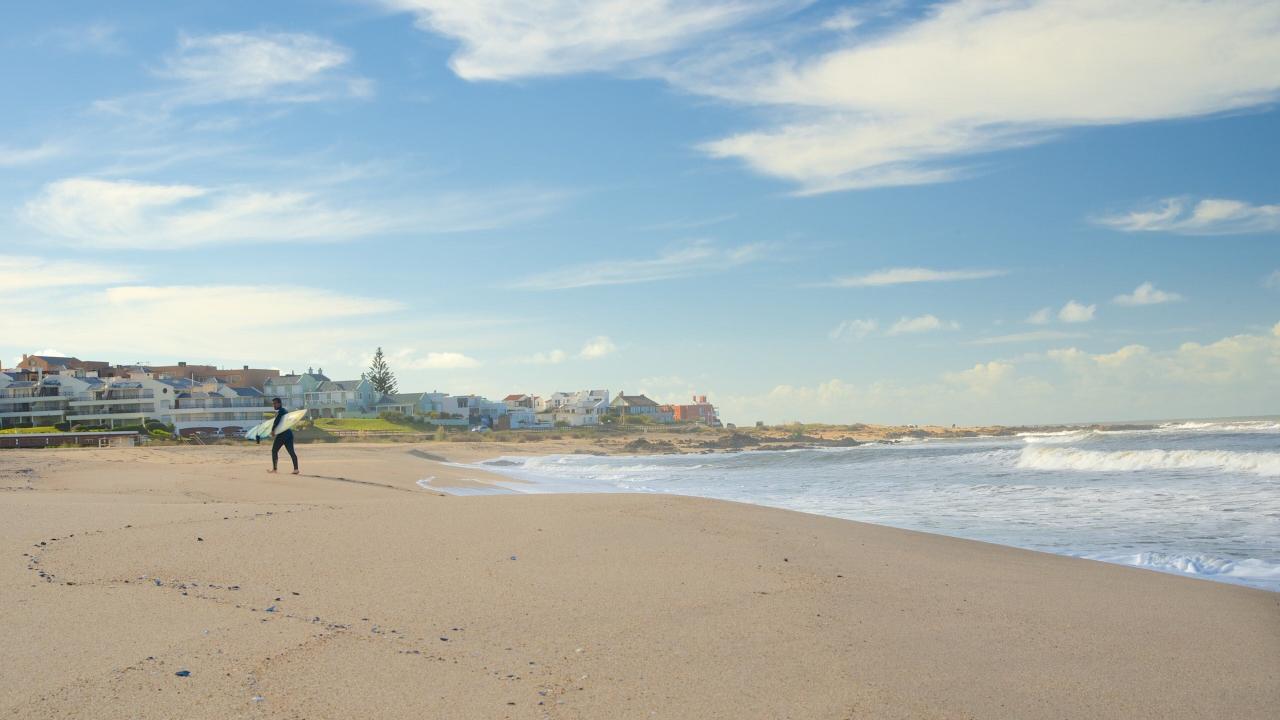 Surfista caminando por la playa del Balneario Honu Beach Mar del Plata