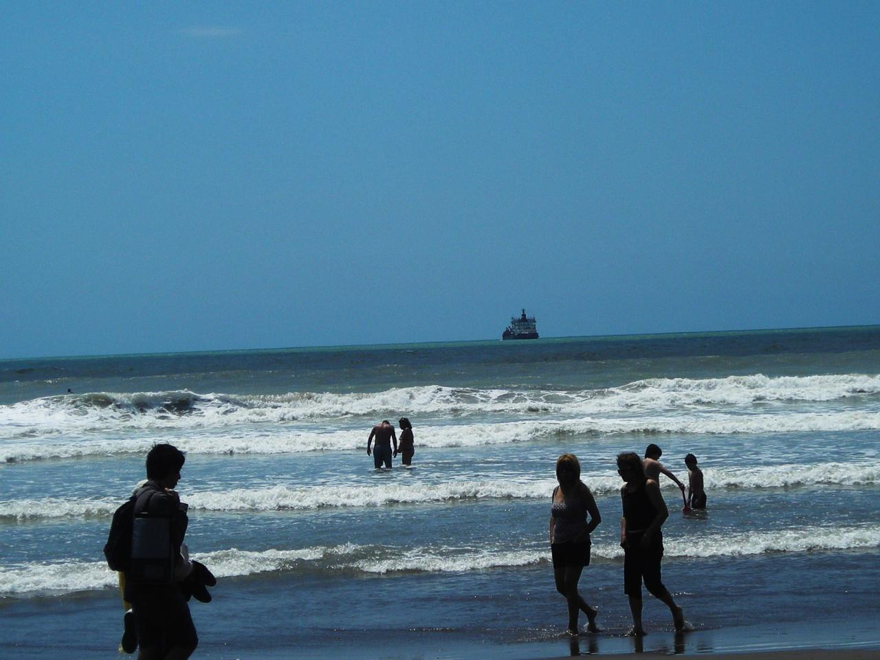 Personas en el agua de Playa Chica Mar del Plata con barco al horizonte