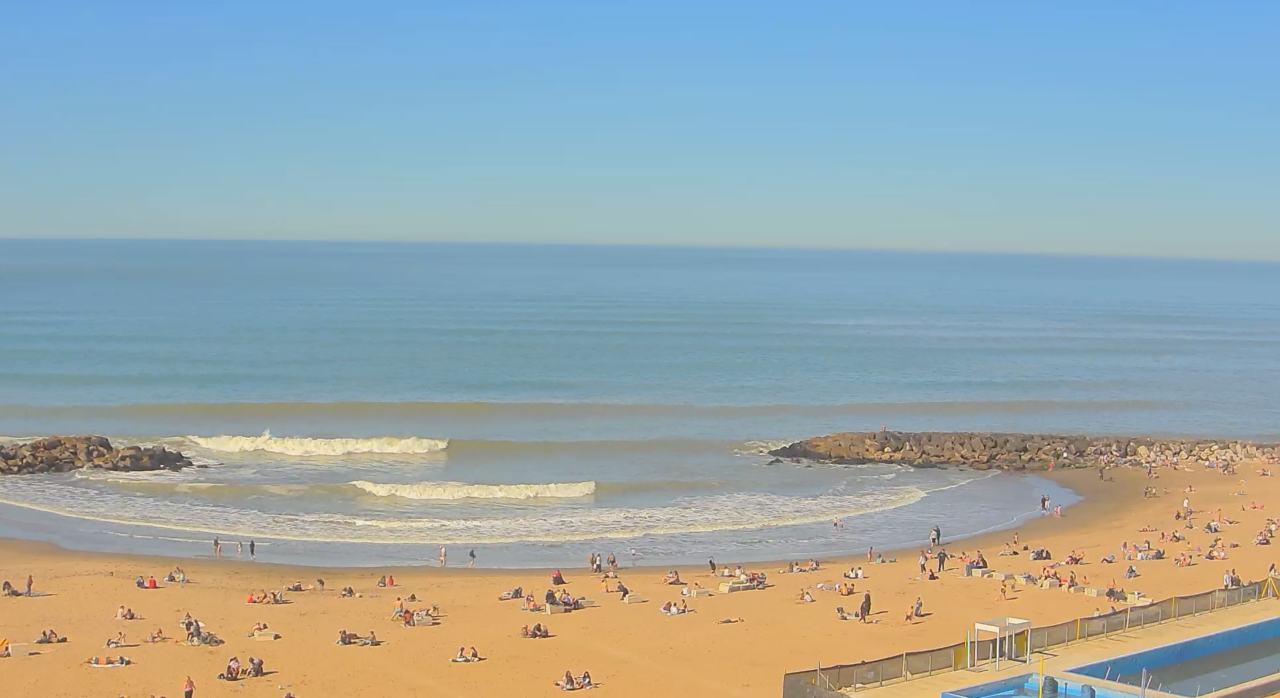 Playa Sun Rider Mar del Plata con surfistas, olas y rompeolas al fondo